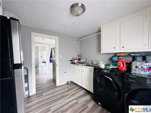 washroom with cabinets, a textured ceiling, sink, light hardwood / wood-style flooring, and washing machine and dryer