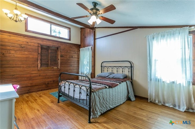 bedroom with wood walls, ceiling fan with notable chandelier, lofted ceiling, and light wood-type flooring