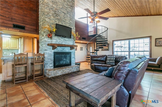 tiled living room with ceiling fan, a stone fireplace, wooden ceiling, and high vaulted ceiling