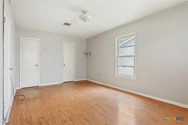 unfurnished bedroom with visible vents, a textured ceiling, baseboards, and light wood-type flooring
