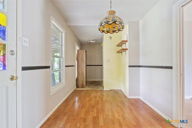 hallway with a textured ceiling, baseboards, and wood finished floors
