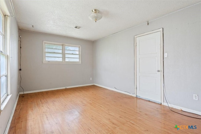 unfurnished room featuring visible vents, baseboards, a textured ceiling, and wood finished floors