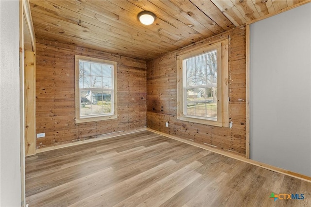 spare room with light hardwood / wood-style flooring, wooden ceiling, wooden walls, and plenty of natural light