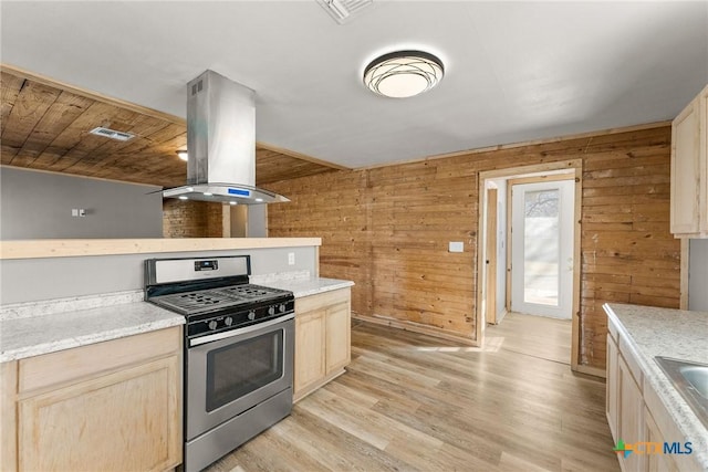 kitchen featuring stainless steel gas stove, wood walls, island range hood, and light hardwood / wood-style flooring