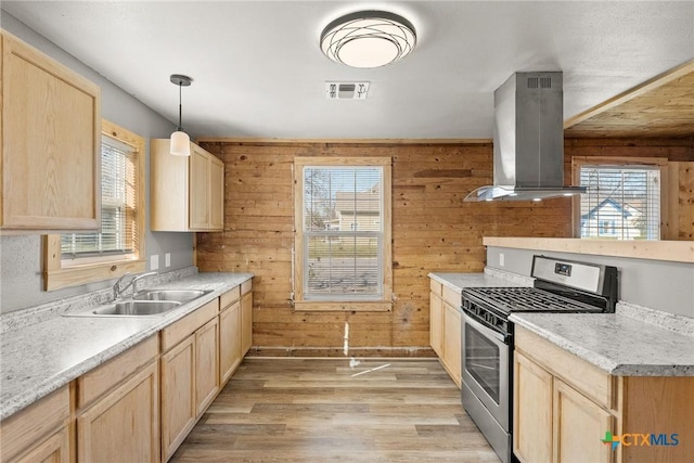 kitchen featuring light hardwood / wood-style flooring, hanging light fixtures, wood walls, island exhaust hood, and gas stove