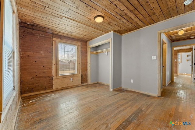 unfurnished bedroom featuring wooden walls, wooden ceiling, a closet, and hardwood / wood-style floors