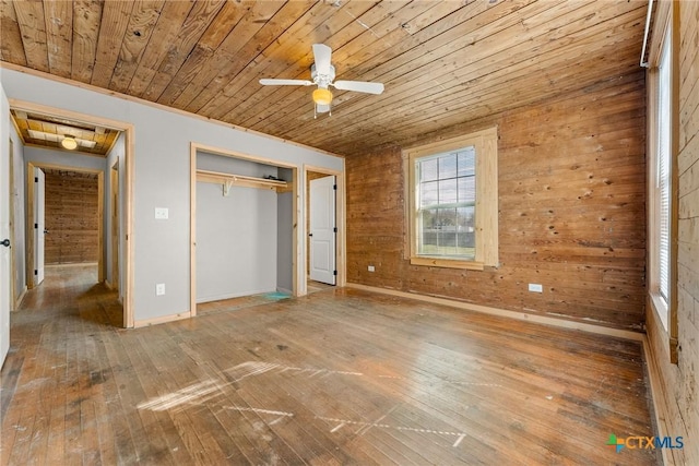 unfurnished bedroom featuring hardwood / wood-style flooring, a closet, wooden walls, wood ceiling, and ceiling fan