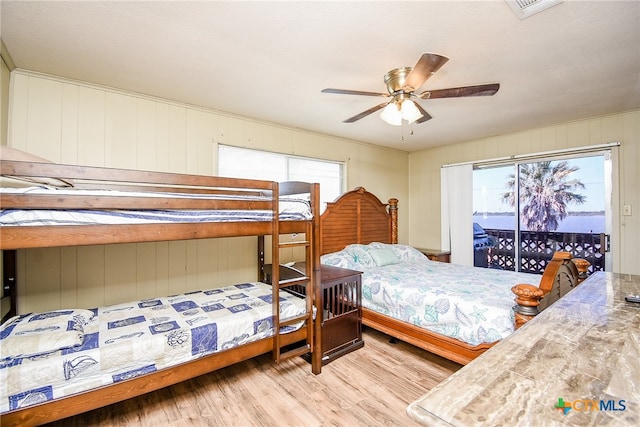 bedroom with light hardwood / wood-style floors, ceiling fan, wooden walls, and access to outside