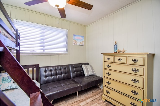 living room featuring wood walls, ceiling fan, light wood-type flooring, and crown molding