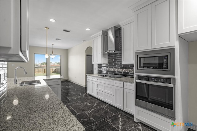 kitchen with light stone counters, built in microwave, wall chimney range hood, white cabinets, and oven