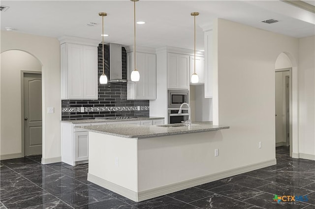 kitchen with light stone countertops, appliances with stainless steel finishes, wall chimney exhaust hood, sink, and white cabinetry