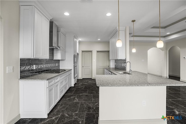 kitchen featuring sink, wall chimney exhaust hood, kitchen peninsula, pendant lighting, and white cabinets