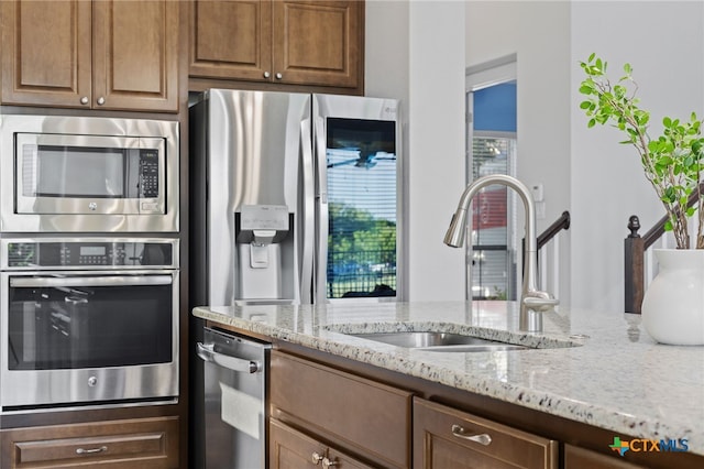 3437 De Soto Loop, Round Rock, TX 78665 - kitchen with stainless steel appliances, a sink, light stone counters, and brown cabinetry
