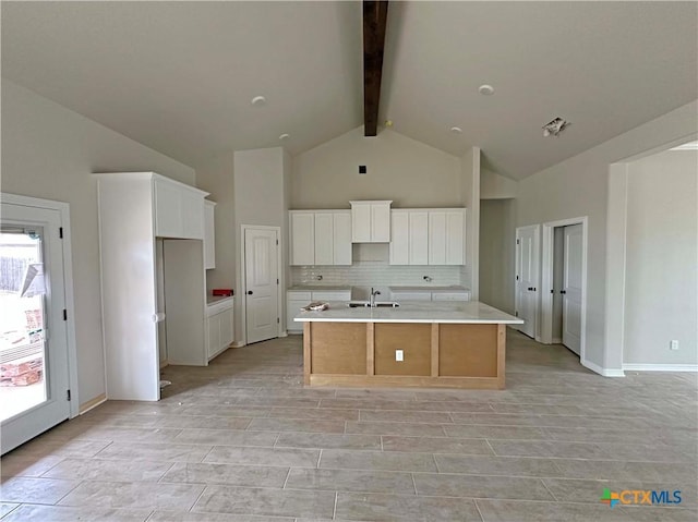 kitchen featuring white cabinets, a large island, beamed ceiling, light countertops, and a sink