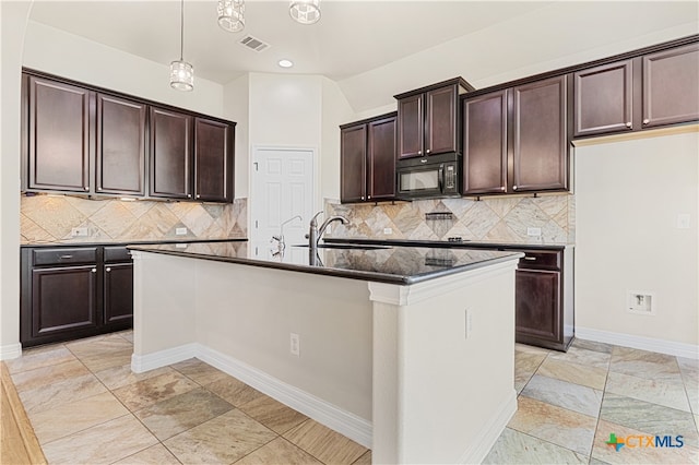 kitchen with backsplash, a center island with sink, dark brown cabinetry, and sink