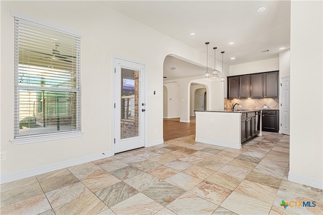 kitchen featuring sink, backsplash, pendant lighting, a center island with sink, and dark brown cabinets