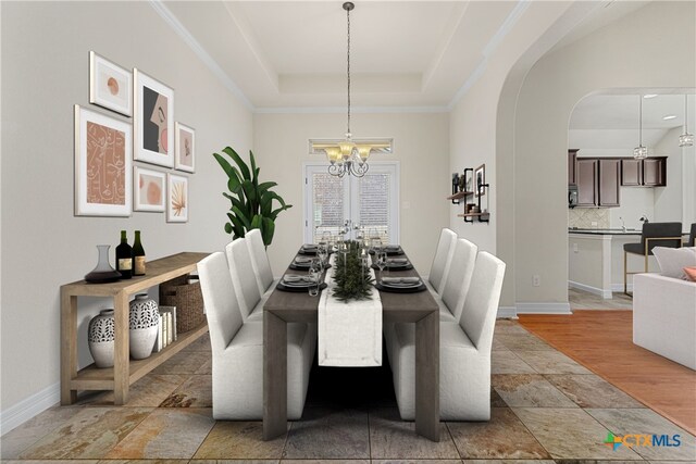 unfurnished dining area with french doors, ornamental molding, a tray ceiling, a notable chandelier, and light hardwood / wood-style floors