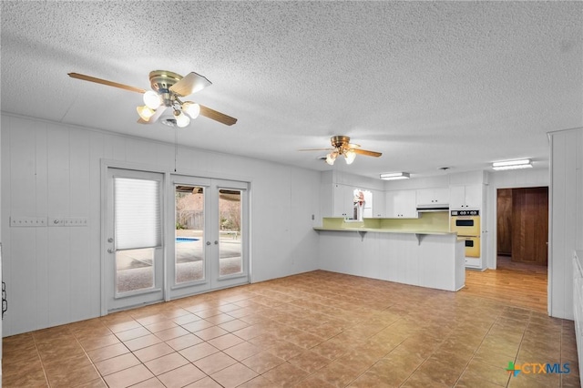 kitchen with ceiling fan, white cabinetry, multiple ovens, a kitchen bar, and kitchen peninsula