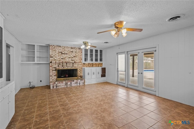 unfurnished living room featuring ceiling fan, a brick fireplace, a textured ceiling, and built in shelves