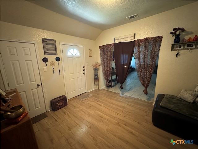 entrance foyer featuring light wood-type flooring, lofted ceiling, and a textured ceiling