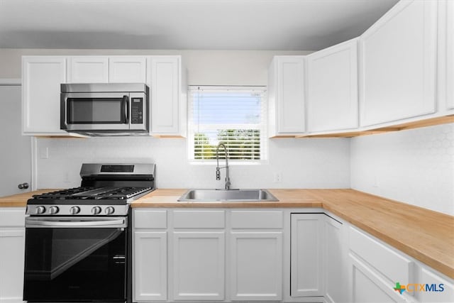 kitchen featuring wood counters, white cabinetry, sink, and gas range