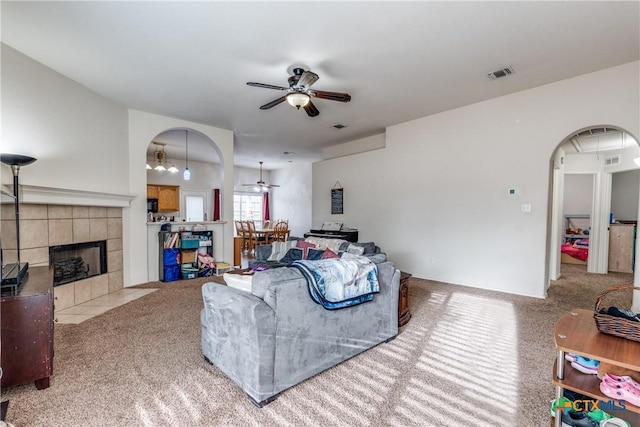 carpeted living room with a tiled fireplace and ceiling fan