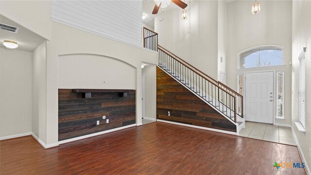 unfurnished living room with ceiling fan, a towering ceiling, and light hardwood / wood-style floors