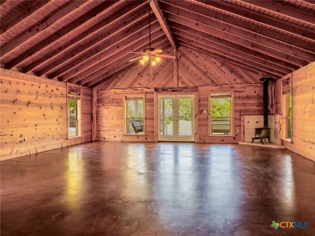 unfurnished living room with concrete floors, a wood stove, wooden walls, wooden ceiling, and ceiling fan