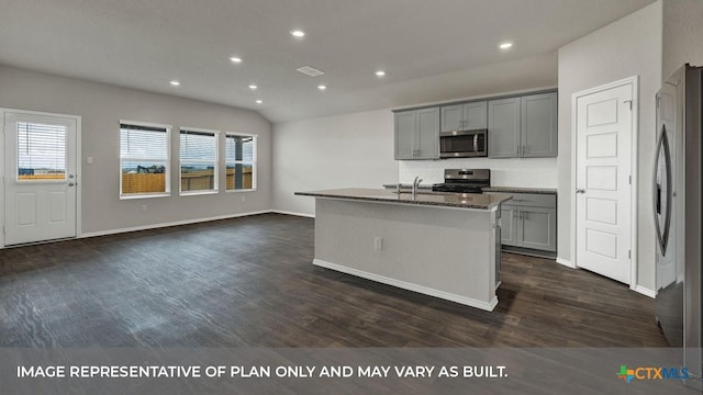 kitchen with gray cabinetry, vaulted ceiling, appliances with stainless steel finishes, dark hardwood / wood-style flooring, and an island with sink