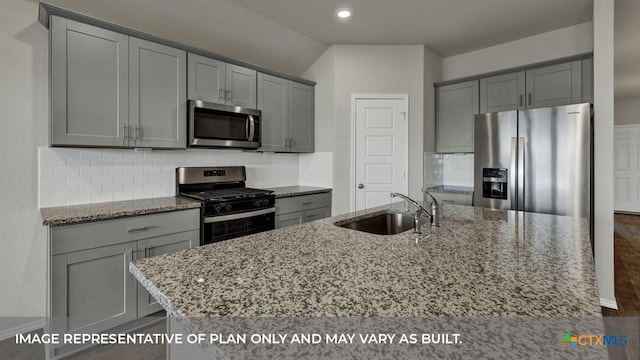 kitchen featuring sink, light stone counters, a center island with sink, appliances with stainless steel finishes, and backsplash