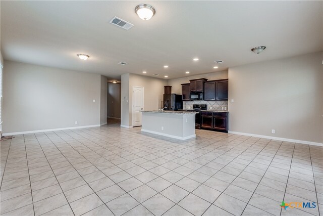 kitchen with dark brown cabinetry, black appliances, light stone countertops, light tile patterned floors, and an island with sink