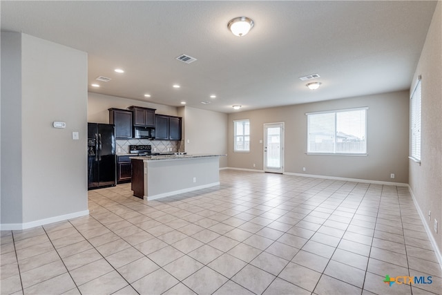 kitchen with a center island with sink, black appliances, light stone counters, light tile patterned floors, and backsplash