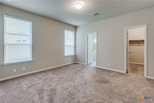 unfurnished bedroom with light carpet, multiple windows, a walk in closet, and a closet