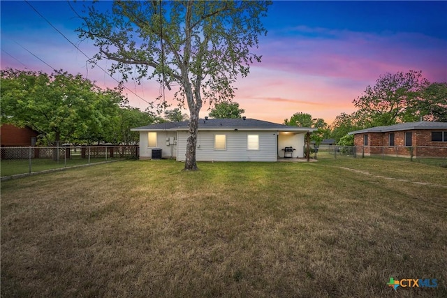 rear view of house with central air condition unit, a lawn, and a fenced backyard