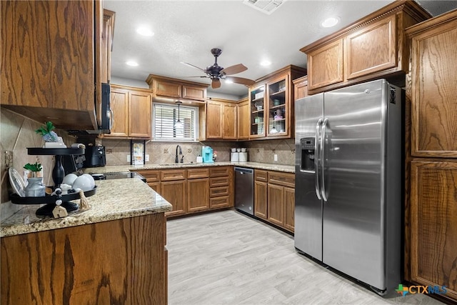 kitchen featuring a sink, brown cabinets, light wood finished floors, backsplash, and appliances with stainless steel finishes