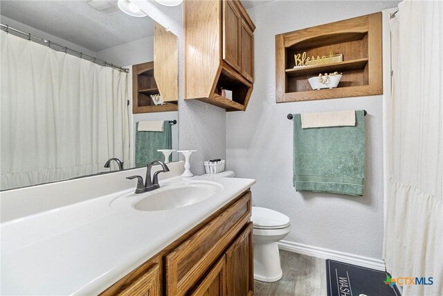 bathroom featuring baseboards, wood finished floors, vanity, and toilet