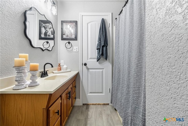 bathroom with a textured wall, a shower with shower curtain, vanity, and wood finished floors