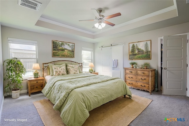 carpeted bedroom featuring a tray ceiling, a barn door, ceiling fan, and ornamental molding