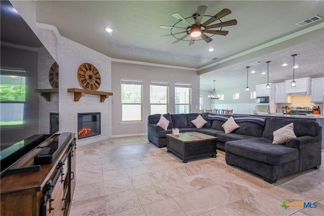 living room with a fireplace, a textured ceiling, ceiling fan with notable chandelier, and crown molding