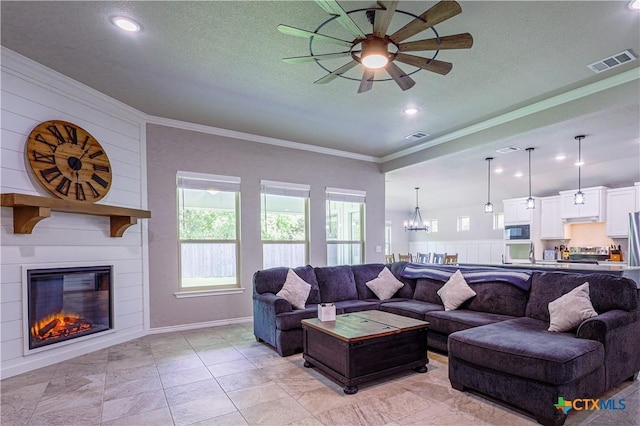 living room with ornamental molding, ceiling fan with notable chandelier, a textured ceiling, a large fireplace, and sink