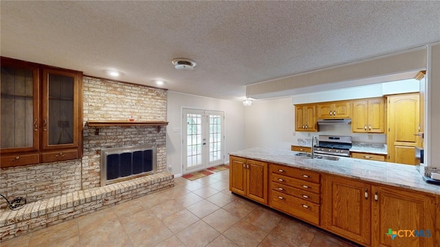 kitchen with french doors, light stone counters, a textured ceiling, stainless steel range oven, and a fireplace