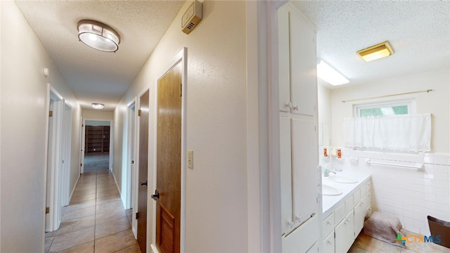 hall featuring a textured ceiling, tile walls, light tile patterned floors, and sink