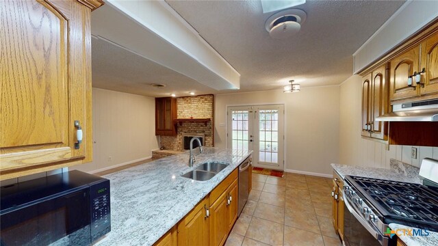 kitchen with stainless steel appliances, light stone counters, a textured ceiling, sink, and light tile patterned floors