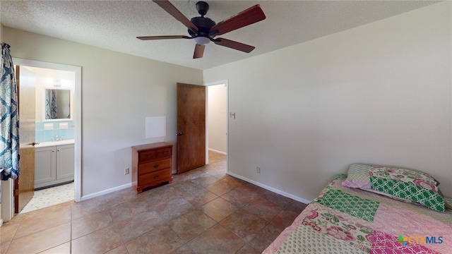 tiled bedroom featuring sink, a textured ceiling, ceiling fan, and ensuite bathroom