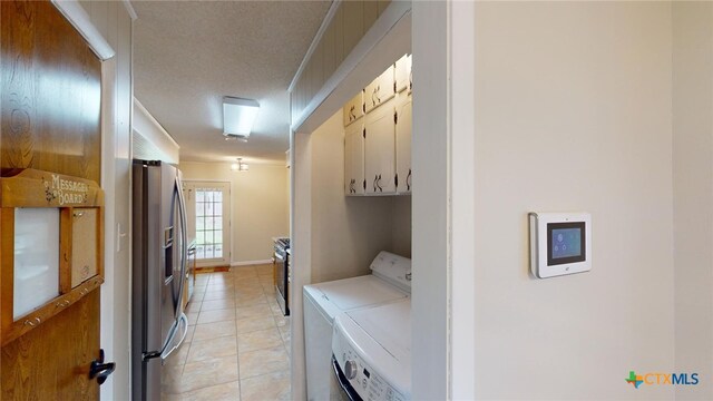 laundry area featuring washing machine and clothes dryer, light tile patterned flooring, cabinets, and a textured ceiling