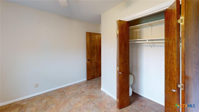 unfurnished bedroom featuring a textured ceiling, light tile patterned floors, ceiling fan, and a closet