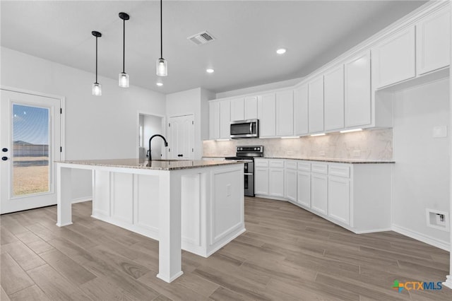 kitchen featuring pendant lighting, white cabinetry, backsplash, stainless steel appliances, and a center island with sink