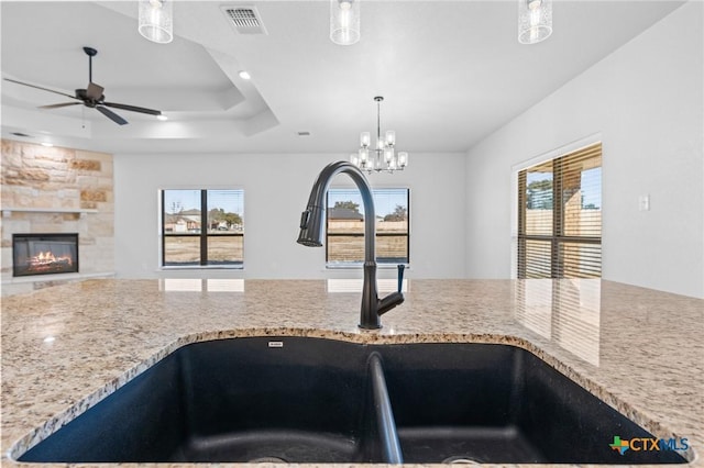 kitchen with sink, hanging light fixtures, ceiling fan, a raised ceiling, and light stone countertops