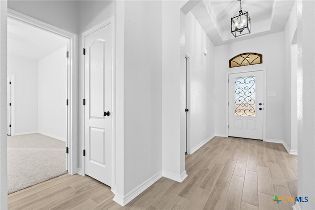 entrance foyer featuring a raised ceiling, a notable chandelier, and light wood-type flooring