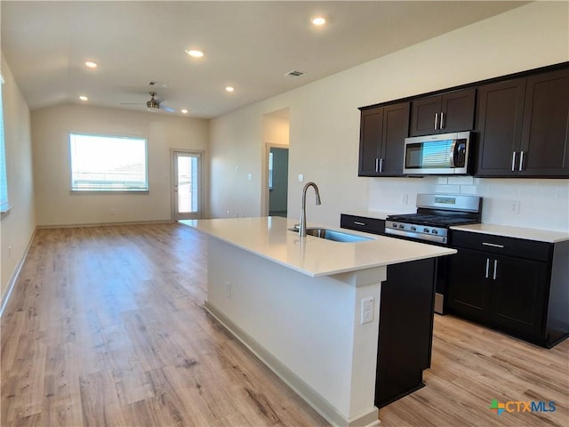 kitchen featuring vaulted ceiling, an island with sink, sink, light hardwood / wood-style floors, and stainless steel appliances